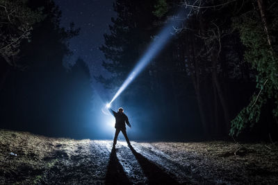 Silhouette woman standing on illuminated street amidst trees at night