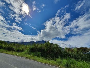 Road by trees on field against sky