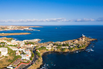 Aerial view of townscape by sea against blue sky