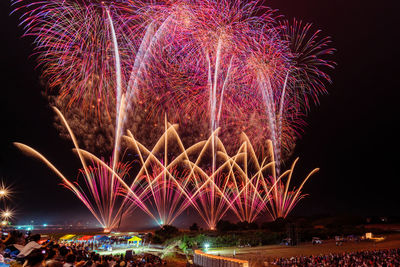 Firework display over illuminated city against sky at night