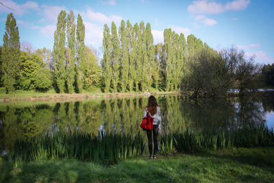 Rear view full length of woman standing against calm lake with reflection