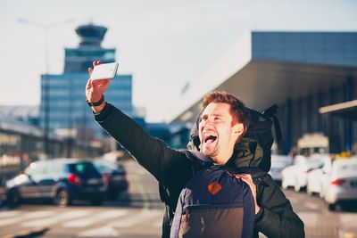 Happy young man taking selfie from mobile phone outside airport