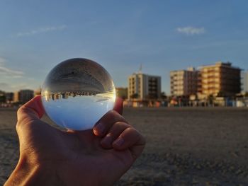 Close-up of hand holding glass of building against sky