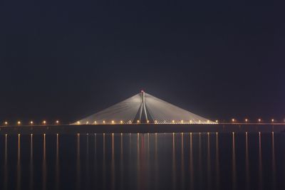 Illuminated bridge over sea against clear sky at night