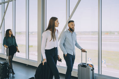 Business colleagues pulling luggage while walking in corridor at airport