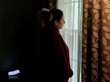 Rear view of woman looking through window at home