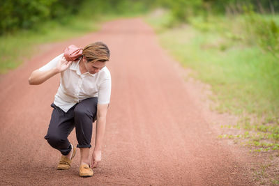 Young man adjusting shoe on dirt road