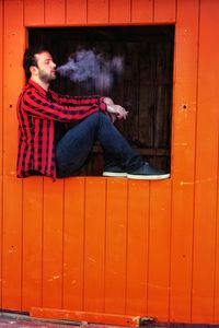 Man smoking cigarette while sitting on red window