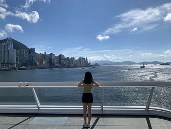 Rear view of woman looking at sea against cityscape