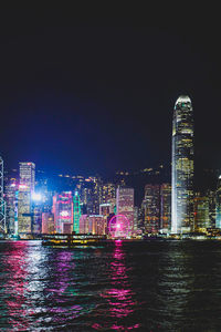 Illuminated buildings by river against sky at night