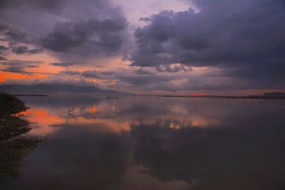 Scenic view of lake against cloudy sky during sunset