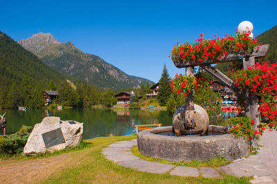 Fountain by lake against clear blue sky in village