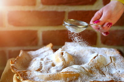 Cropped hand of woman dusting powdered sugar on pie