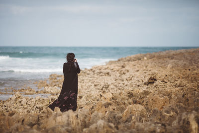Rear view of woman photographing on beach 