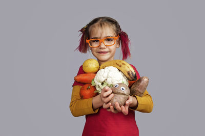 Portrait of smiling girl holding camera against gray background