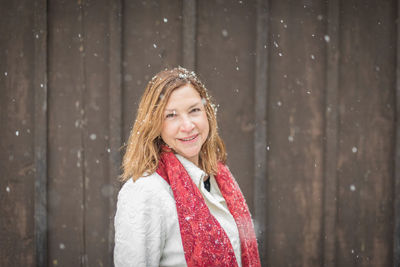 Portrait of smiling woman wearing warm clothing against wooden wall during winter