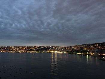 Illuminated cityscape by sea against sky at night