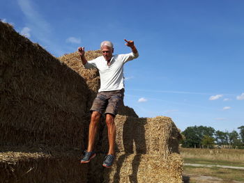 Full length of man jumping from hay stack on field against sky