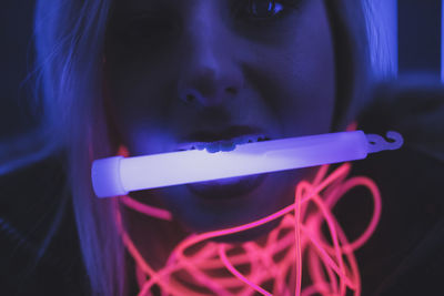 Woman in hooded clothing carrying equipment in mouth standing against illuminated lights