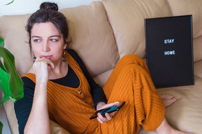 High angle view of woman with phone sitting on sofa at home