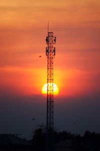 Silhouette of communications tower against orange sky