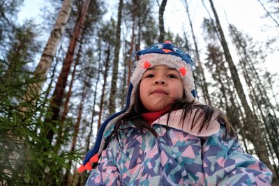 Portrait of cute girl in warm clothes against trees during winter