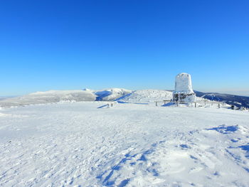 Snow covered landscape against clear blue sky