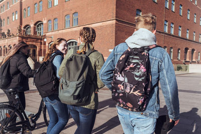 Rear view of teenage friends walking together on footpath in city