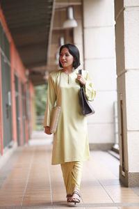 Thoughtful woman holding purse while walking in corridor