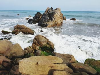Rocks on shore by sea against sky