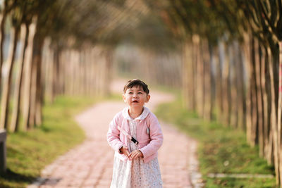 Cute girl standing on footpath amidst trees