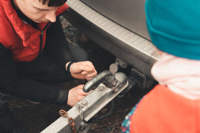 Man connects a trailer to the towbar of his car, and a child watches the process. 