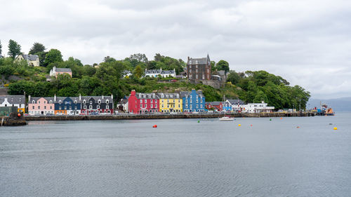 Buildings by sea against cloudy sky