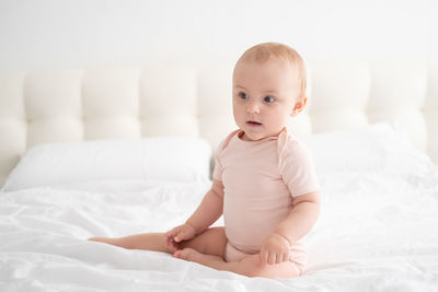 Cute baby girl sitting on bed at home