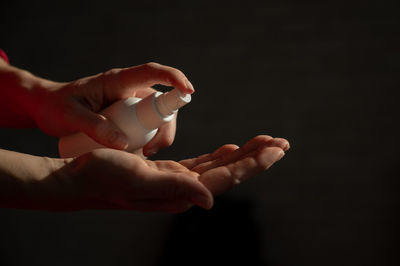 Cropped hand of person holding pills against black background