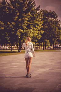 Woman skateboarding on footpath against trees