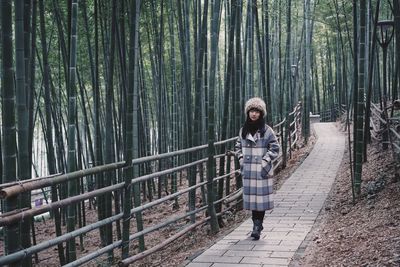 Full length of woman wearing warm clothing standing on footpath at forest