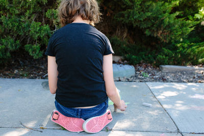 The back of a girl sitting on the sidewalk wearing shoes with wheels