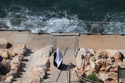 Rear view of man walking on steps by railing against sea