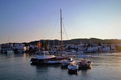 Sailboats moored in harbor at sunset