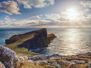 Neist point lighthouse on rocky cliff above wavy sea. blue evening sea and sharp cliffs, scotland
