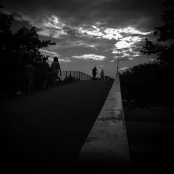 People walking on road against cloudy sky