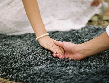 Cropped image of bridegroom holding hand of bride on carpet 