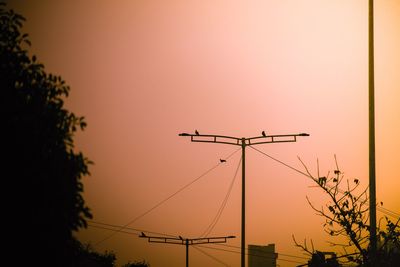 Low angle view of silhouette electricity pylon against sky during sunset