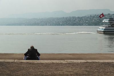 Rear view of senior man sitting by sea against sky