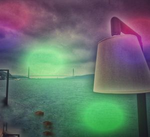 Digital composite image of illuminated lamp on sea against sky at night