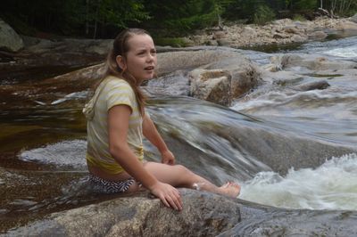 Teenage girl sitting on rock in river