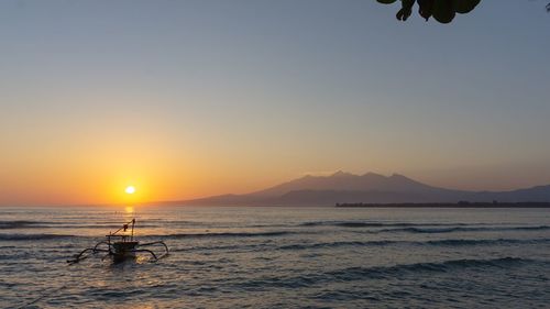 Outrigger in sea against sky during sunset