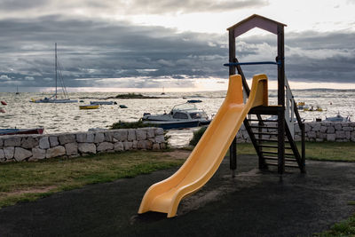 Empty slide at playground by sea against cloudy sky