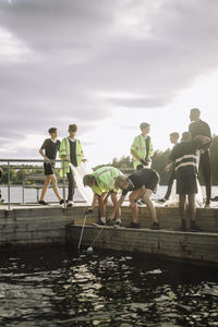 Boys cleaning lake from jetty against sky